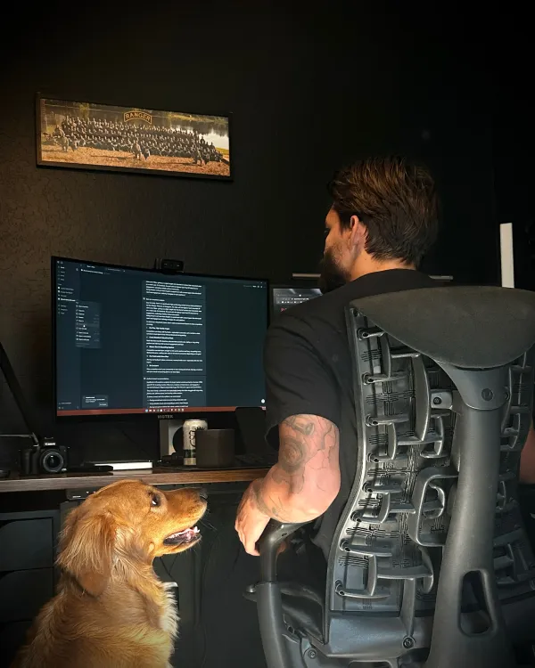 Web developer working at a dual-monitor desk setup with a golden retriever by his side